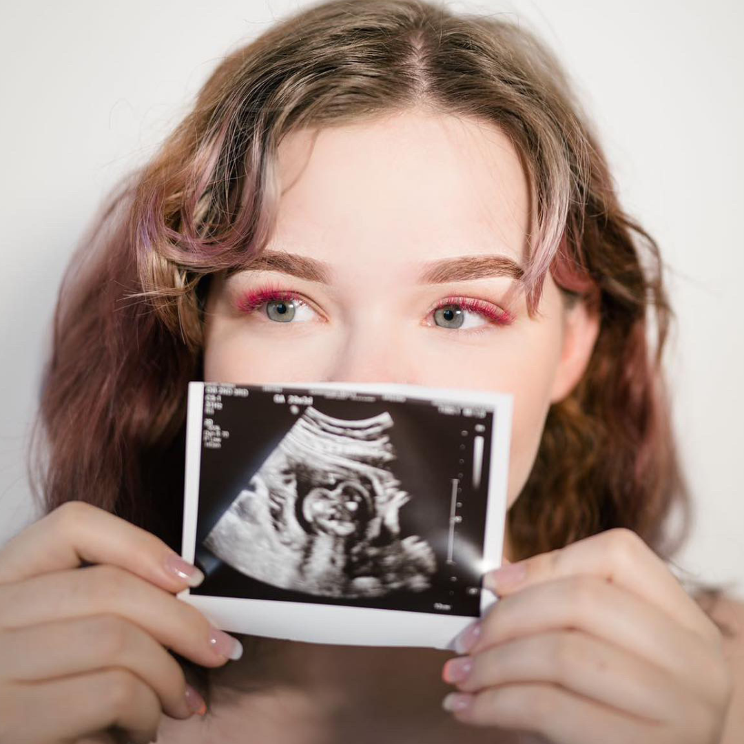 Mother-to-be holds photos of her ultrasound during her Gender Reveal Eyelash Extensions photoshoot